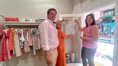 Amaia del Campo, Alberto Ruiz y la responsable del comercio Juliet, colocan el cartel de la campaña
